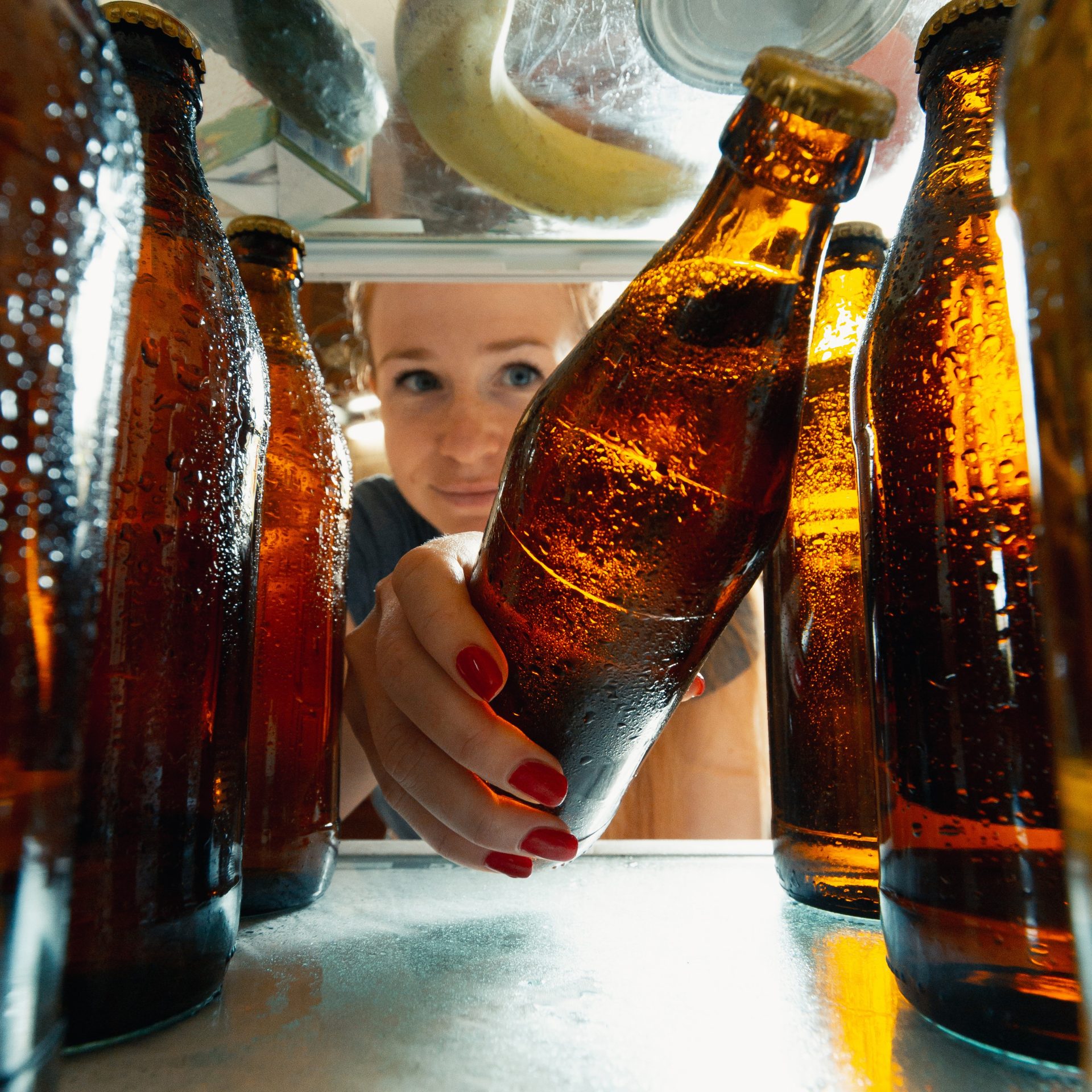 View from inside the refrigerator of a woman putting bottle of beer in the refrigerator.